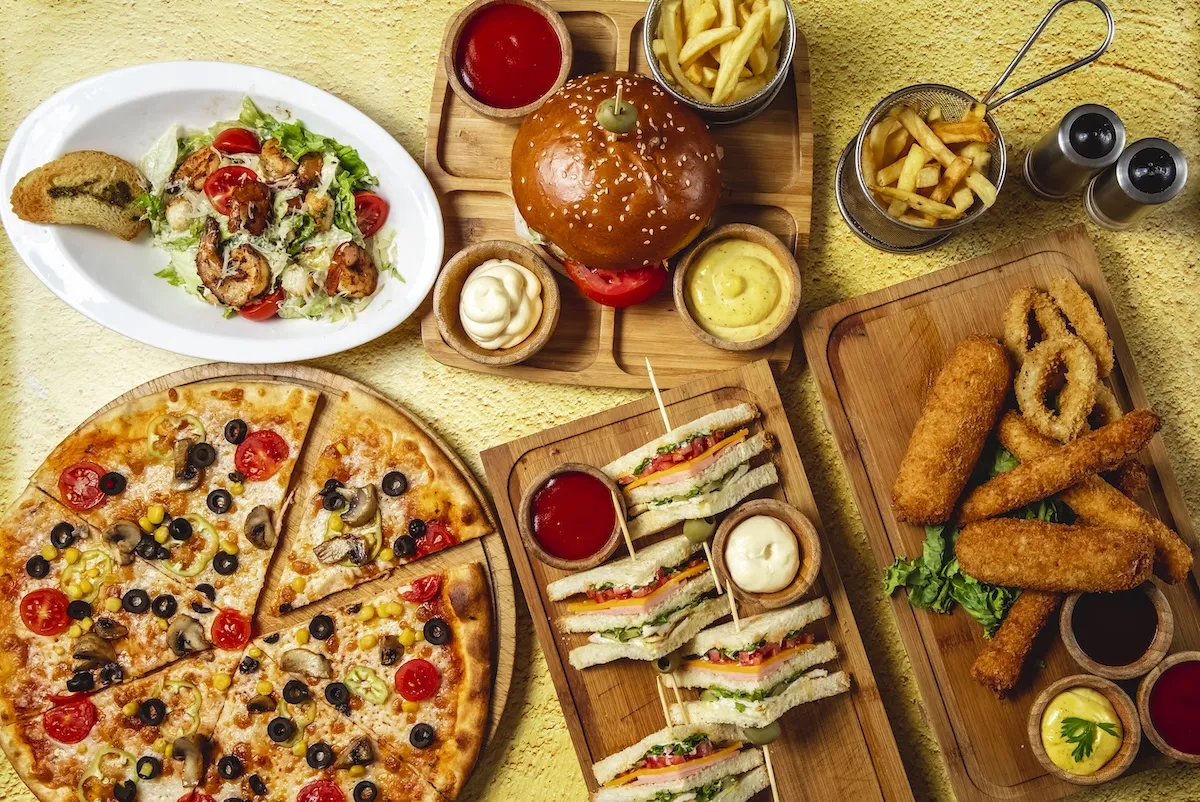 top-view-fast-food-mix-mozzarella-sticks-club-sandwich-hamburger-mushroom-pizza-caesar-shrimp-salad-french-fries-ketchup-mayo-cheese-sauces-table