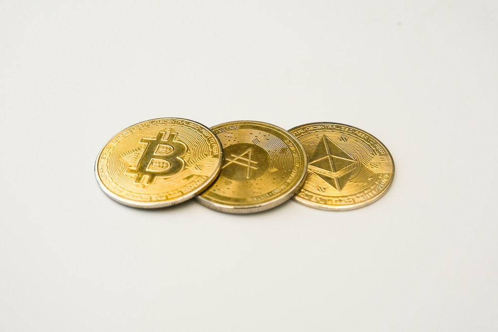 Three gold bitcoins sitting side by side on a white surface